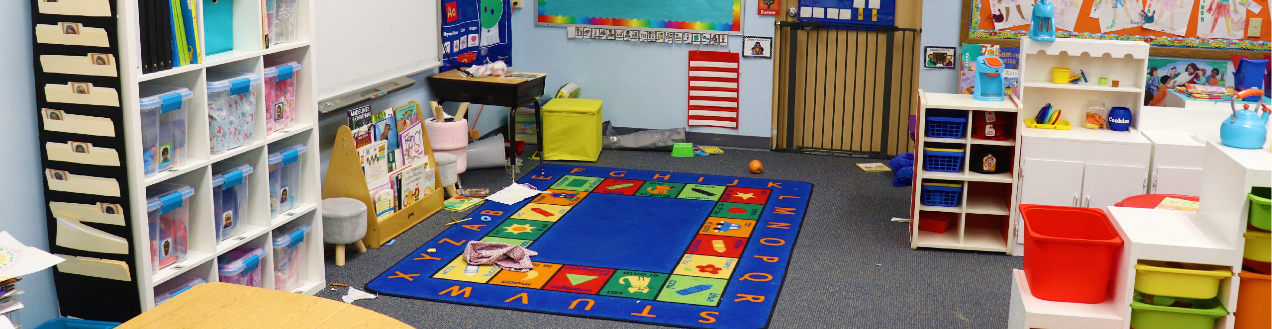 A pre-K classroom is shown with a colorful rug, small bookshelves, and learning stations as an example of a pre-k school facility that might be funded through the State of New Mexico. 